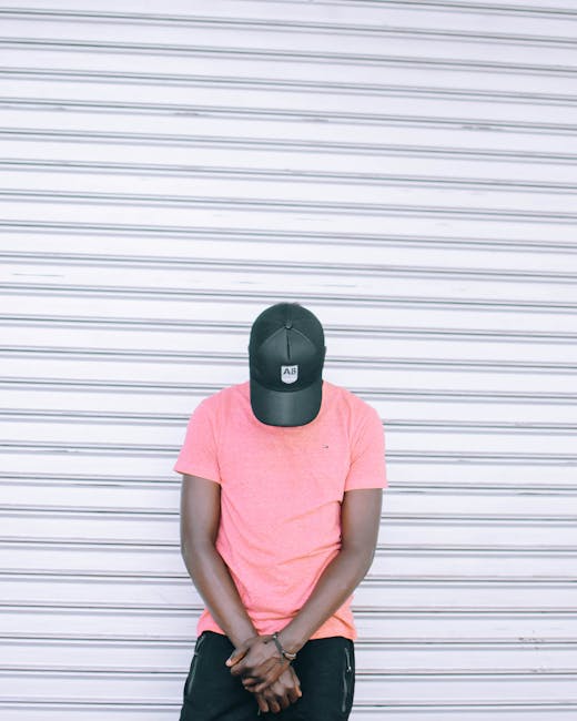 A casual portrait of a man wearing a pink shirt and cap against a striped background.
